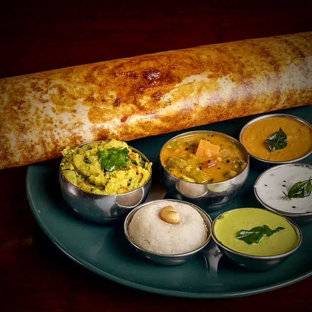 A folded dosai with chutneys and sambar