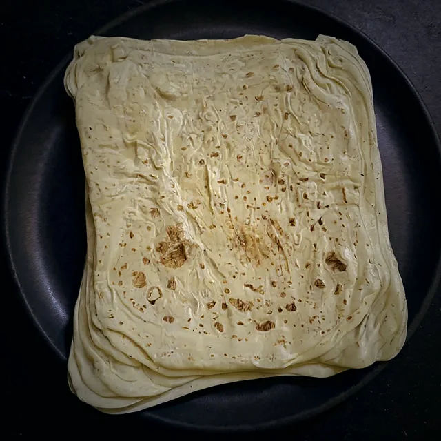 A stack of flaky layered veechu rotti on a dark plate at Restaurant BMS